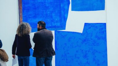 A photograph of two people looking at a large blue abstract painting.