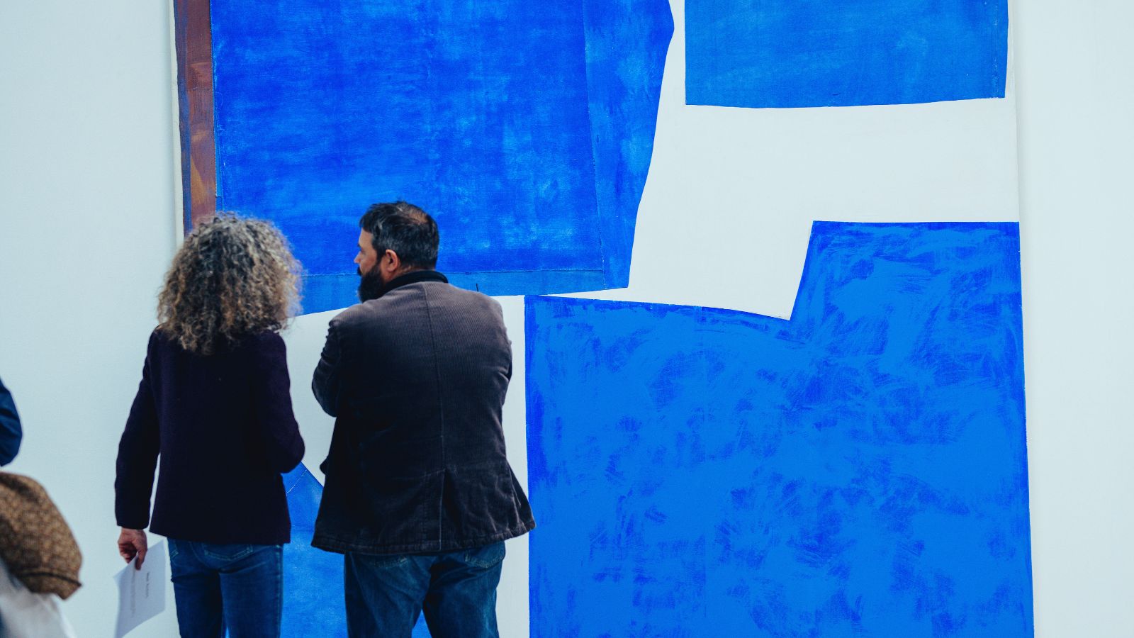 A photograph of two people looking at a large blue abstract painting.